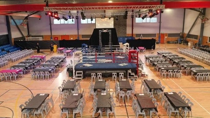 An indoor court set up for a boxing and dinner event, with tables, chairs and a ring in place.