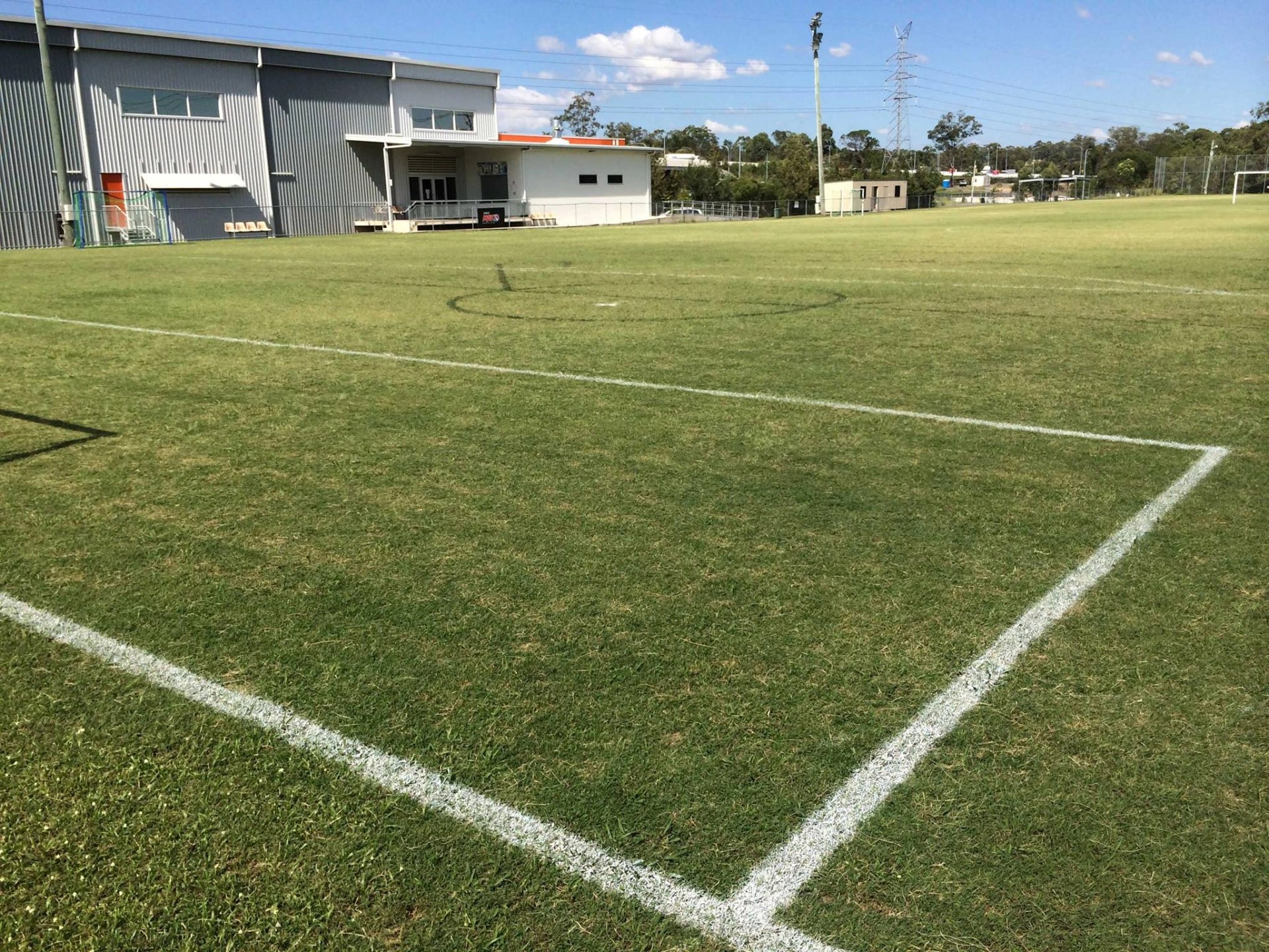 Wide view of one of the outdoor fields at Eagles Sports Complex, showing pitch markings, the grandstand and clubhouse in the background.