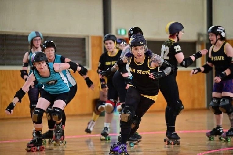 Roller derby players skating hard around the indoor court during a bout.