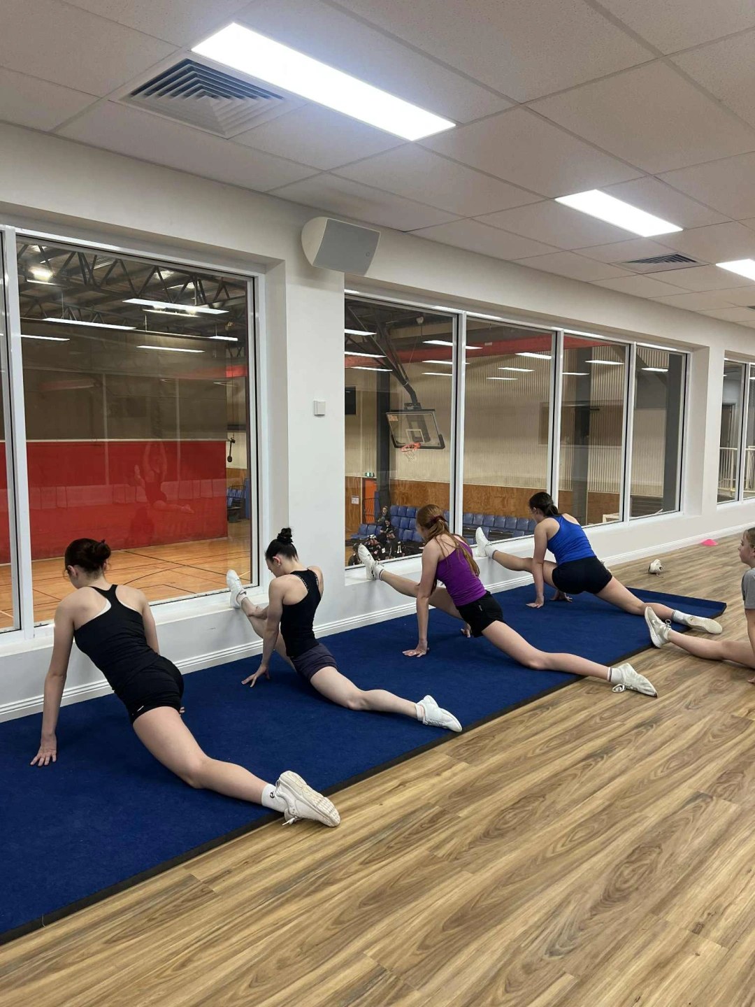 A group stretching class in the upstairs multipurpose room, with a view over the indoor court.
